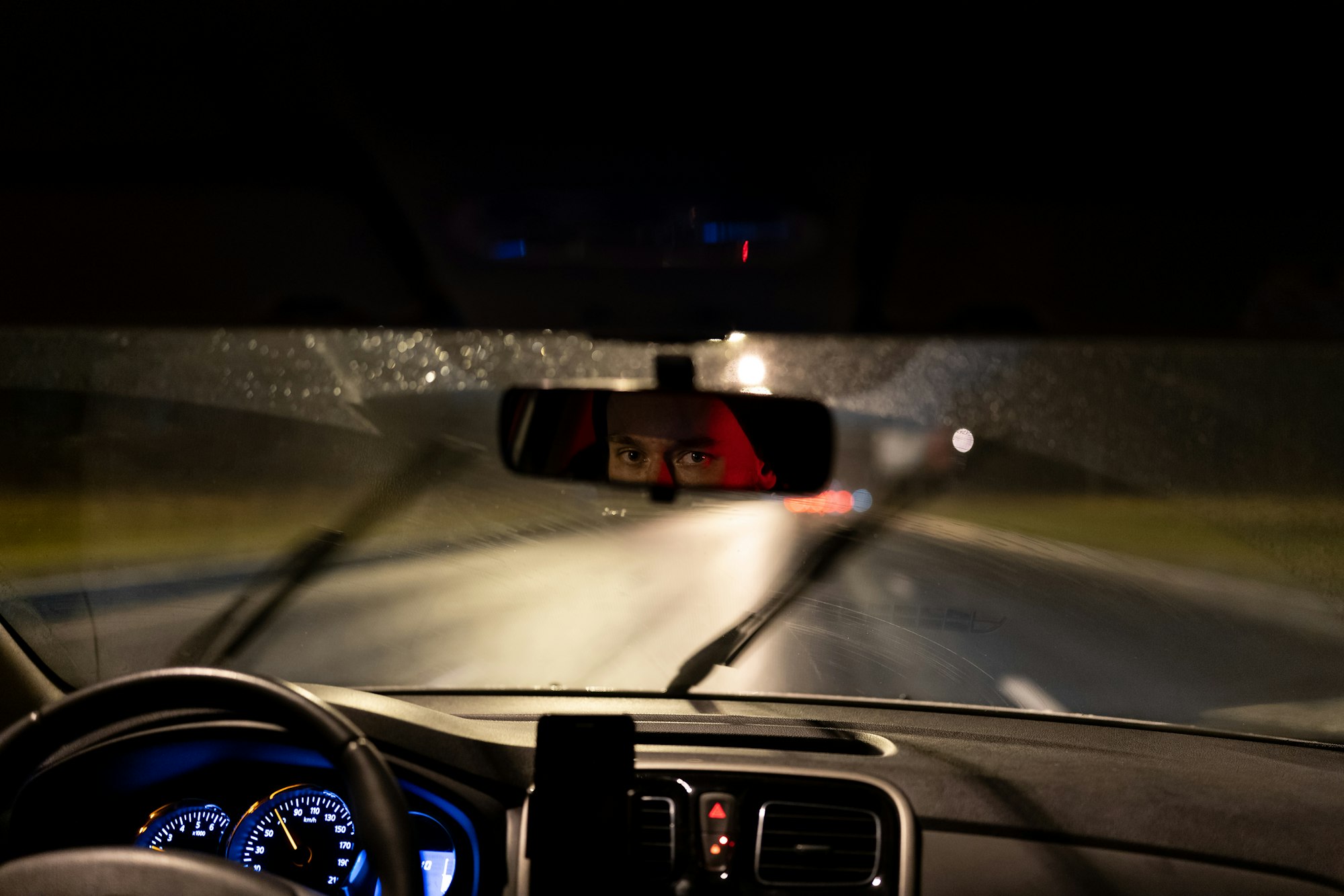 Eyes of young man taxi driver are reflected in rearview mirror during night trip around city